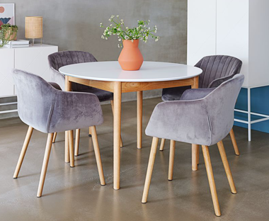 Contemporary round wooden table with white top and oak legs paired with grey upholstered velvet chairs with matching oak legs