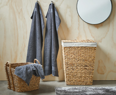 Laundry basket in wicker with two hanging towels behind