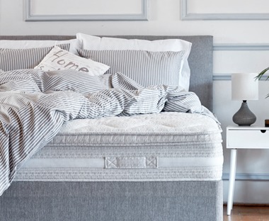 A spring mattress with grey bedding in airy bedroom