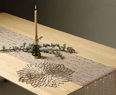 Brown table runner with decorative candle and wreath branch laying across it