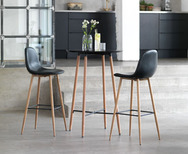 Two black faux leather bar stool with wooden legs placed beside matching bar table with black table top and wooden legs