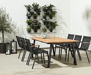 large garden dining table with wooden top and black metal legs paired with black metal garden dining chair 