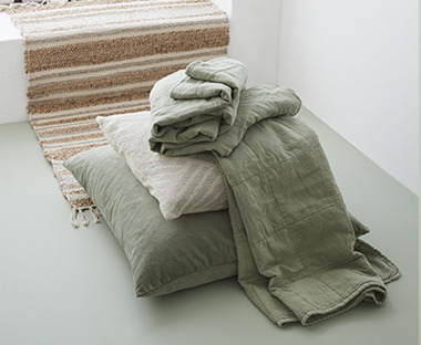 large green floor cushion with smaller beige cushion and green throw piled on top