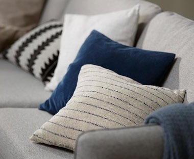 Cushions arranged on a sofa. Beige cushion with black stitching, blue velvet cushion