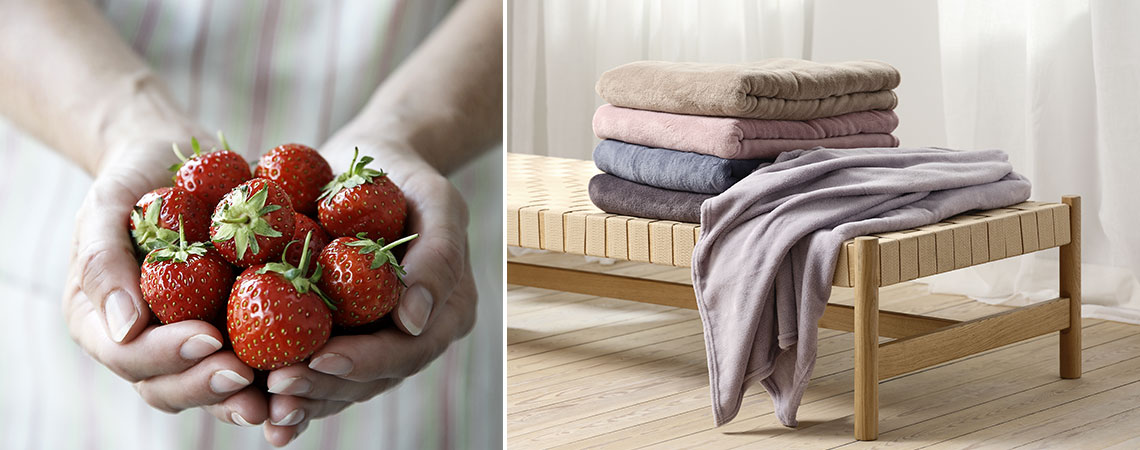 Woman holding fresh strawberries in her hands and a daybed with a stack of throws in summer colours 