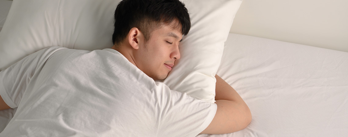 Man sleeping peacefully in bed with white pillow and white mattress topper