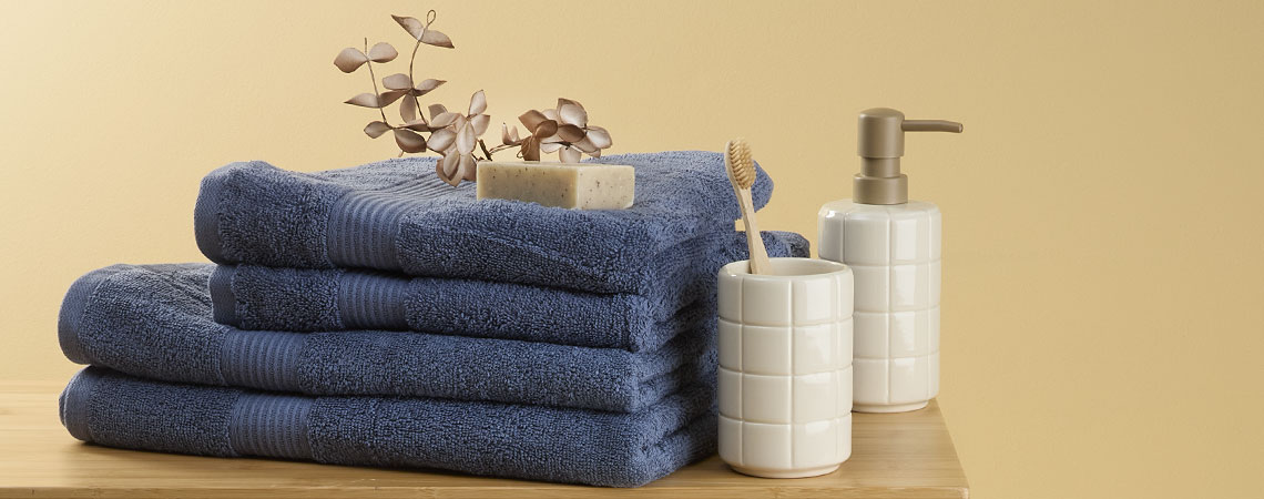 Stack of blue towels on a bench with a toothbrush holder and a soap dispenser 