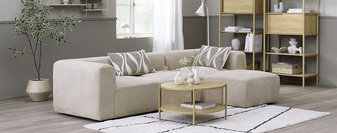 Beige modular sofa in a living room area together with a coffee table, bookcases, and a plant