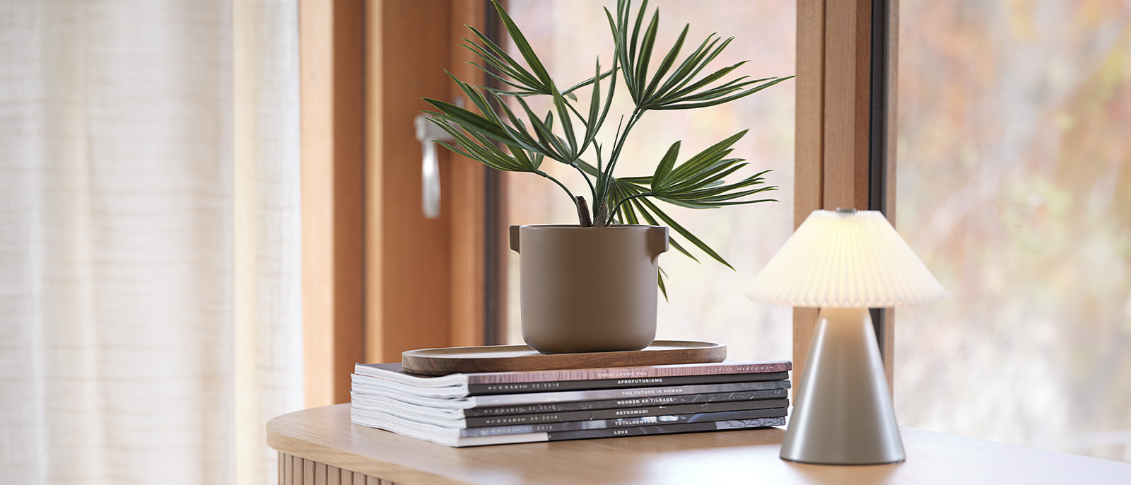 Add a touch of maintenance-free greenery to your home Artificial plant in plant pot on desk with books and table lamp