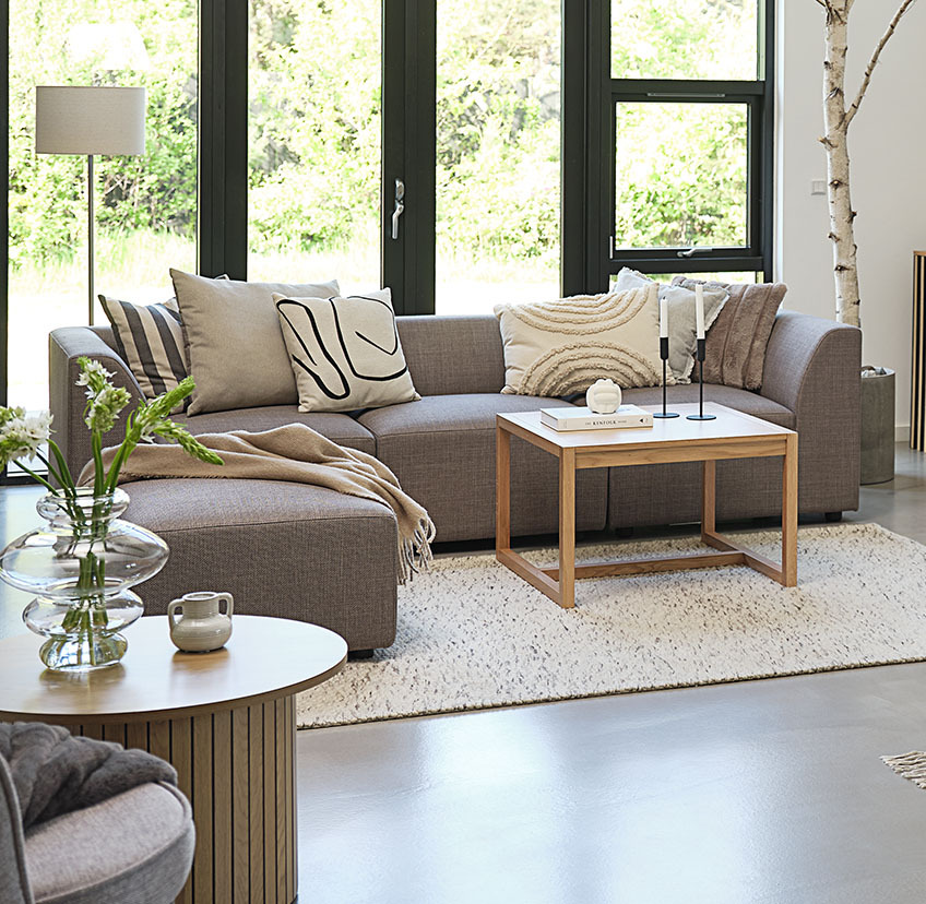 Minimalistic oak coffee table in bright living room with large sofa and decorative cushions 