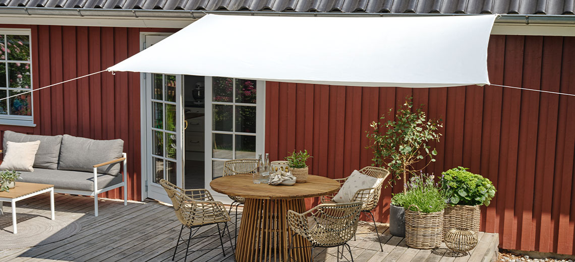 Large shade sail in white above patio with garden table and garden chairs