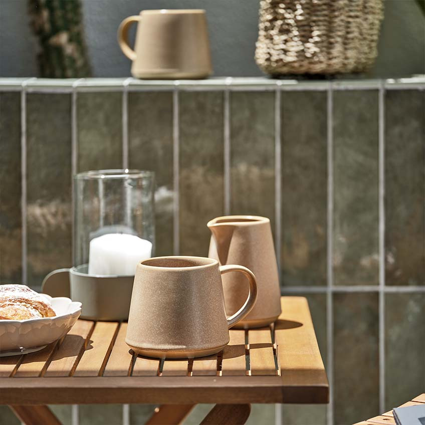 Coffee mug and milk jar on small wooden garden table in full sun 
