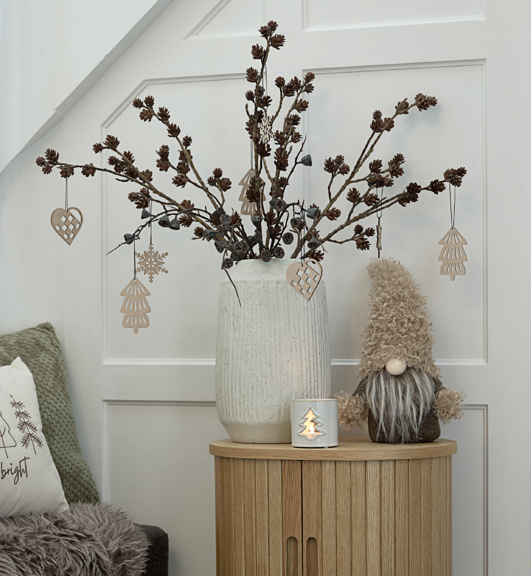 A small table with a vase of Christmas decorations and a Christmas elf beside it