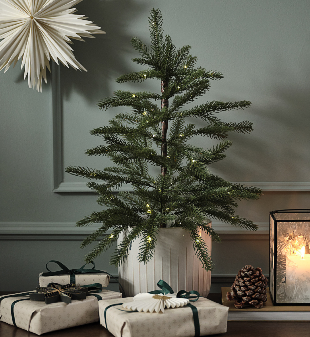 Artificial Christmas tree in a pot with lights and a paper star on the wall 