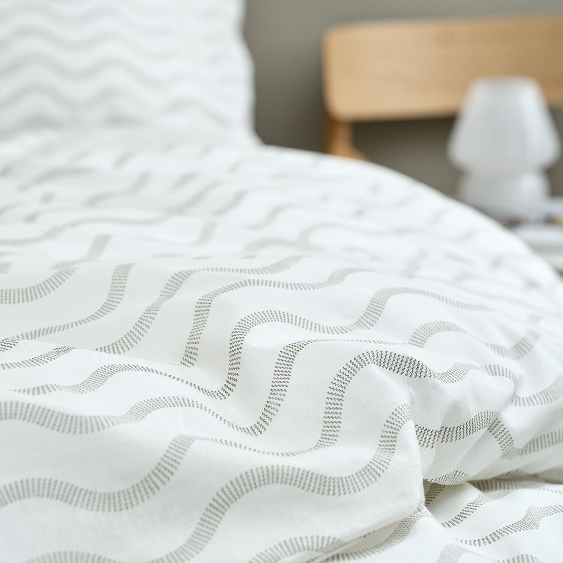 Closeup of white cotton bedding with wave pattern in olive green