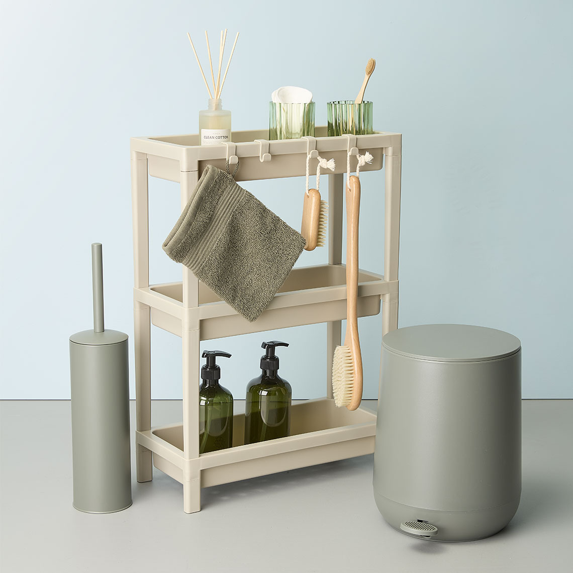 A shower storage in plastic with a washing glove and bath brushes placed next to a toilet brush and a toilet bin