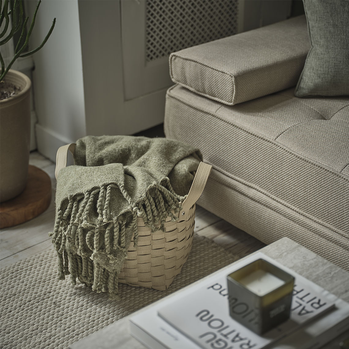 Green throw in a basket standing next to a beige daybed