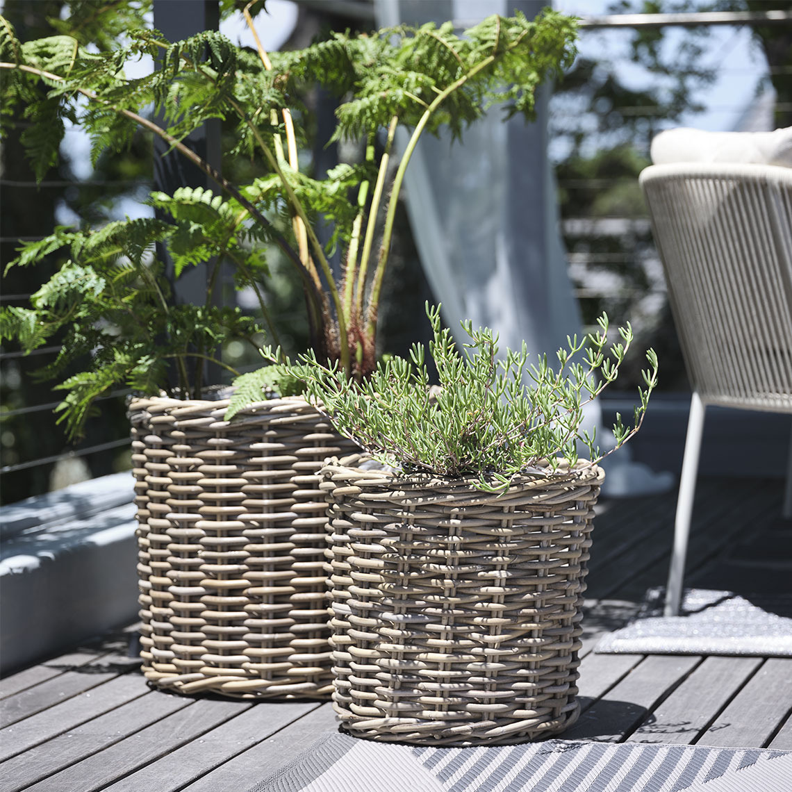 SEGLA planter baskets Two planter baskets in natural, untreated rattan standing on a balcony with plants