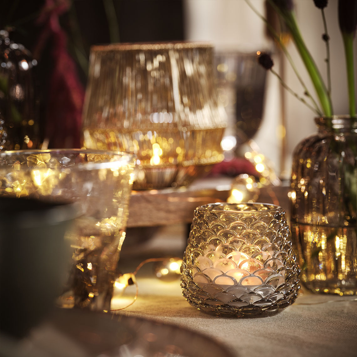 Dining table lit up by candles and tealights in tealight holders and string lights 