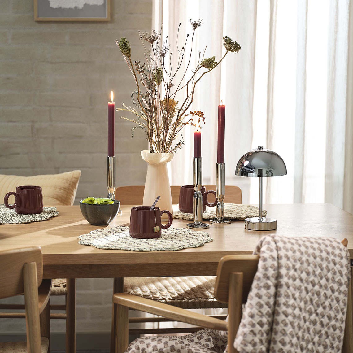 Dining table with bowl, mugs, placemats, vase, candlesticks and battery lamp
