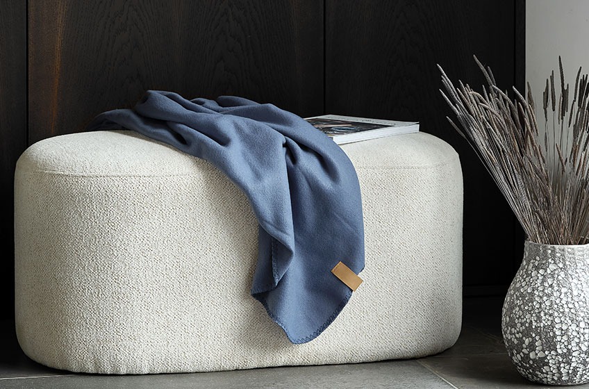 OREBO pouffe with blue DAGLILJE throw. To the left the MATHIAS vase Off-white pouffe with a blue throw on top beside a grey and white vase