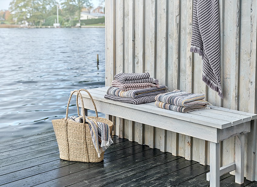 Luxury towels on a bench and in a wicker bag by a lake