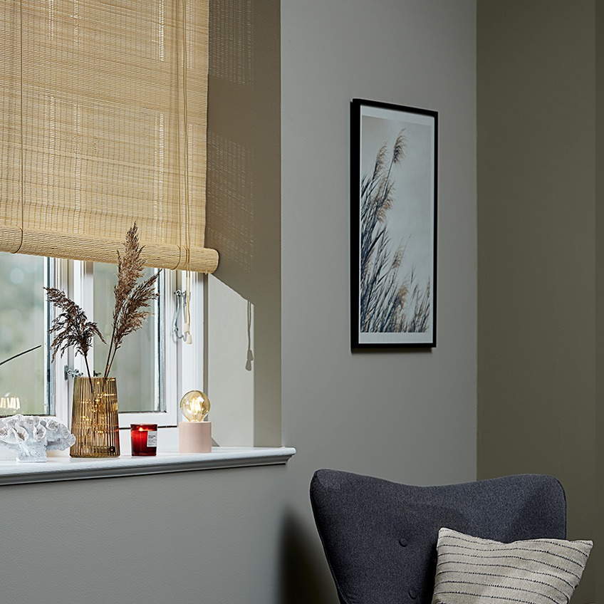 Bamboo roller blinds in a window with a vase, a scented candle and a battery lamp in the windowsill