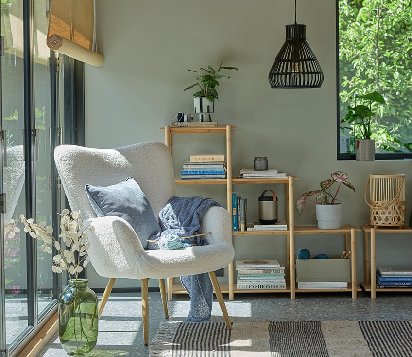 Grey armchair by a window with a green floor vase and a bamboo room divider in the background