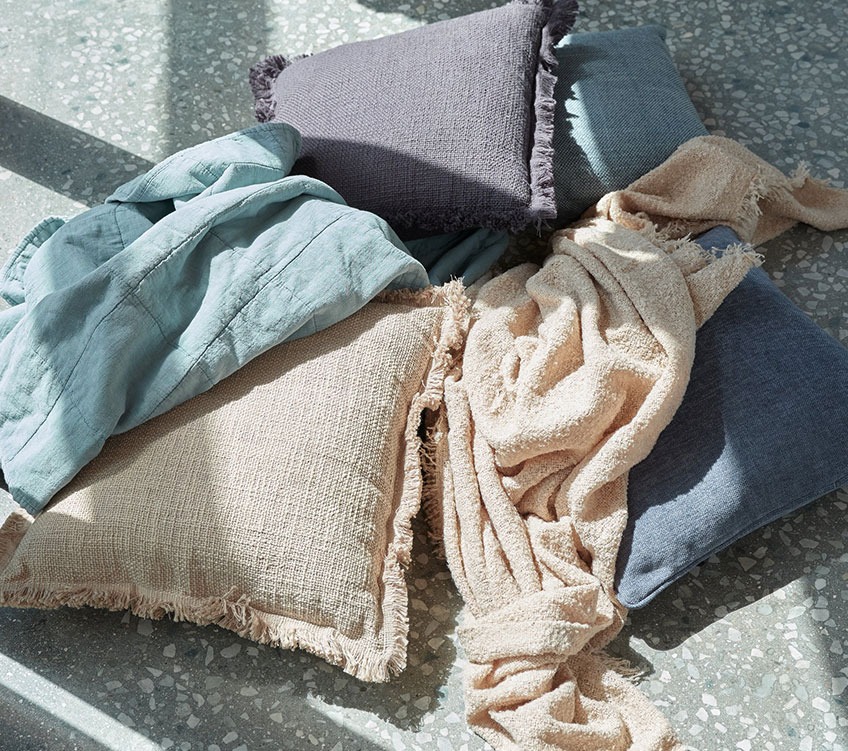 Blue throw, beige throw, and khaki and blue cushions on the floor 