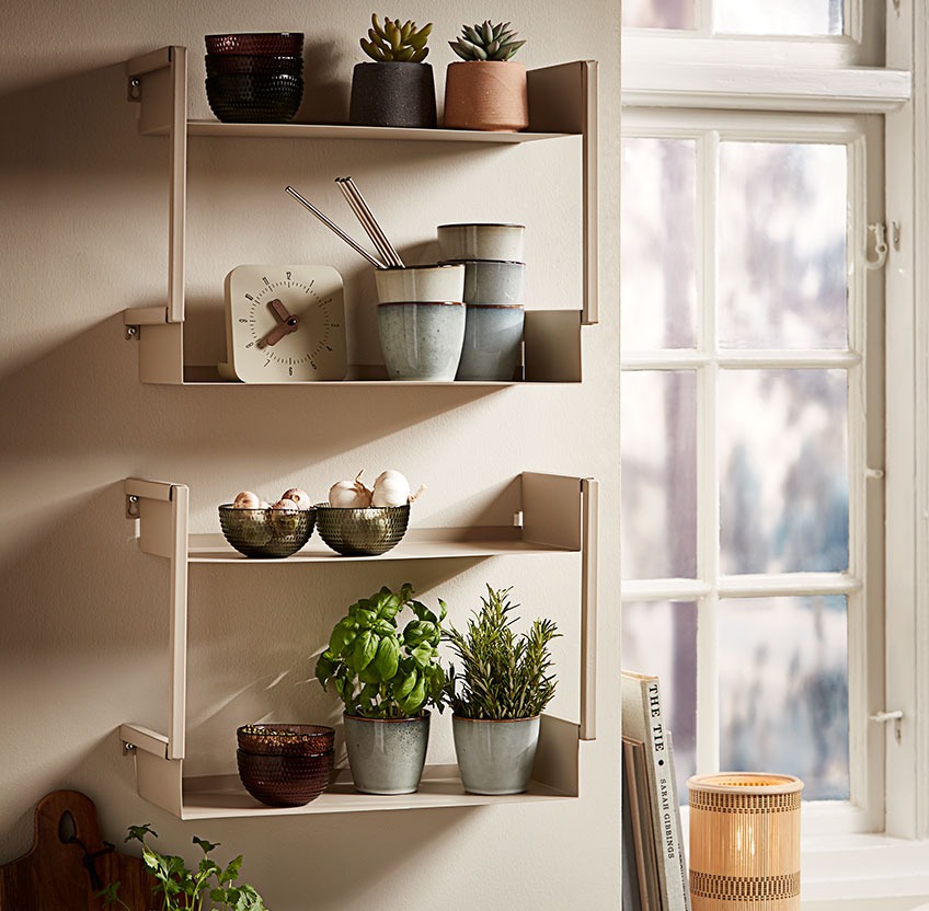 Glass bowls, stoneware mugs and fresh herbs on a wall shelf in a kitchen