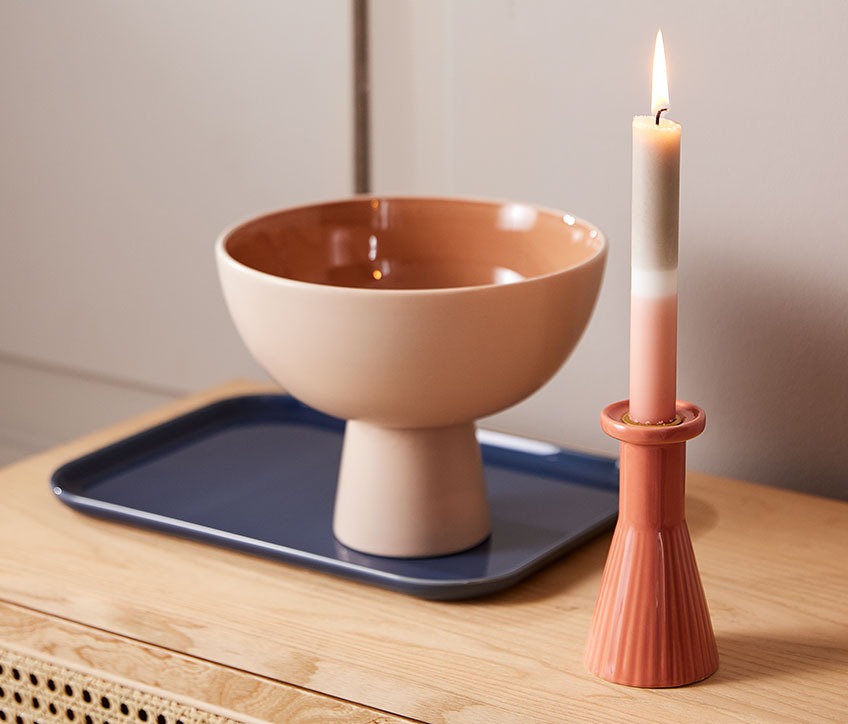 Bowl on a serving platter, beside a candlestick with a striped candle 