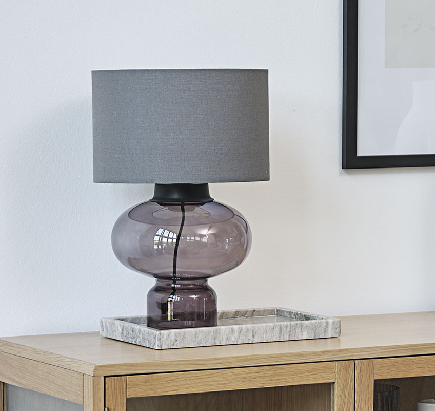 Table lamp with glass base and grey lampshade on a marble tray
