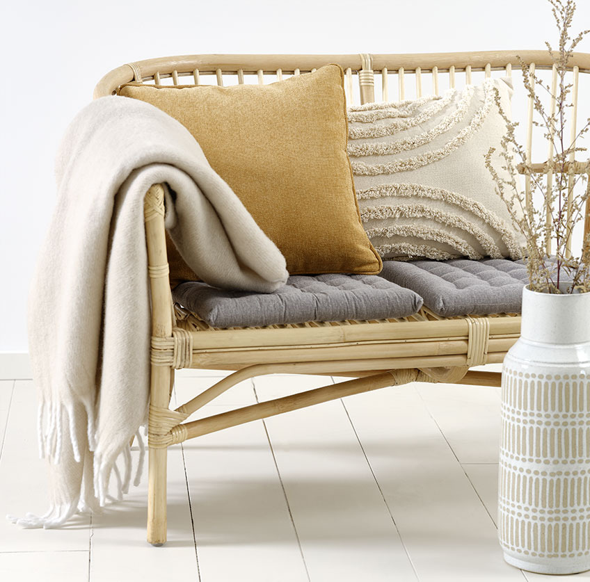 Rattan sofa with beige and yellow cushions and beige throw 