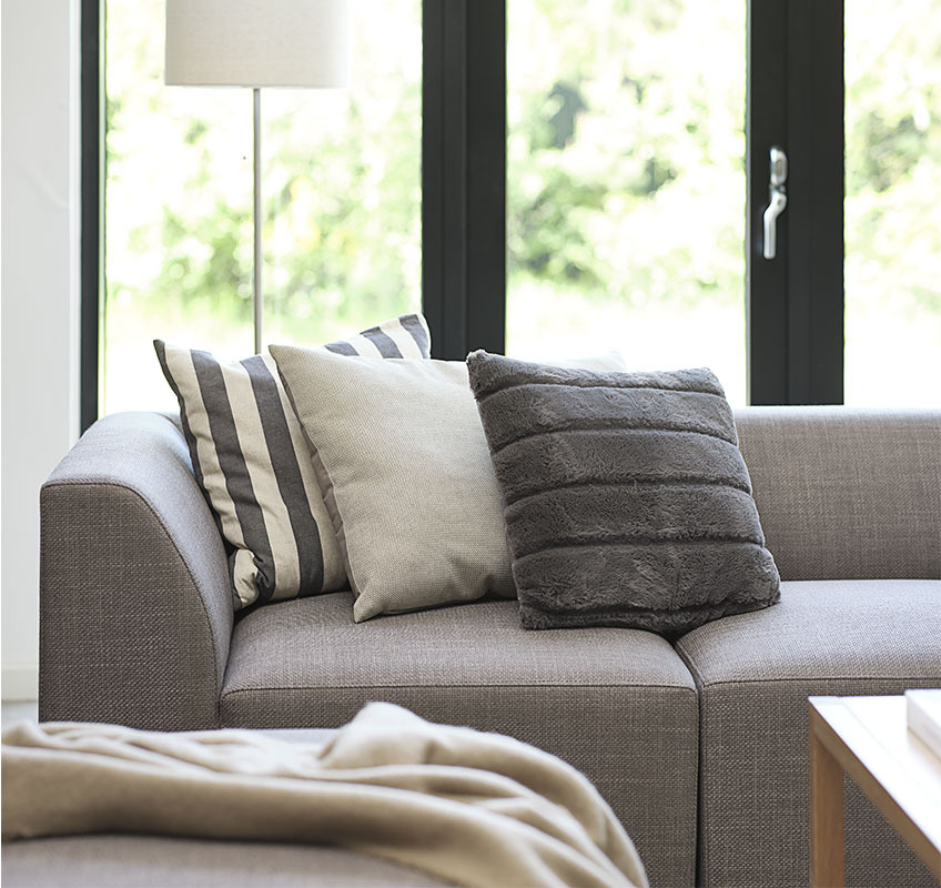 Grey modular sofa with three decorative cushions in Scandinavian living room